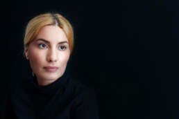 Portret profesional al unei femei cu păr blond prins, îmbrăcată în negru, pe fundal închis