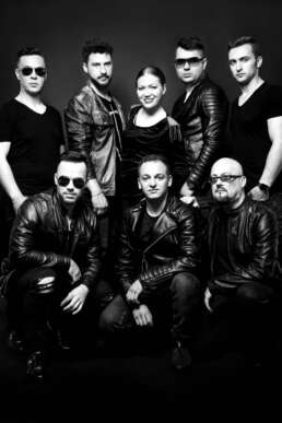 Portret de studio alb-negru al trupei Artizan – 8 membri în ținute rock, pe fundal închis