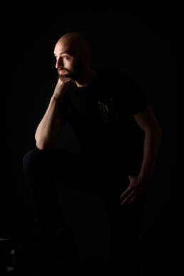 Portret bărbat creativ, lumină dramatică, fundal negru, fotografie artistică tip corporate, expresie gânditoare