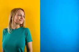 Portret profesional al unei femei blonde, realizat în studio, cu fundal colorat galben și albastru. Fotografie corporate modernă, ideală pentru LinkedIn, website-uri profesionale sau branding personal.