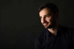 Portret profesional masculin realizat în studio, iluminare laterală artistică, fundal închis. Stil elegant și relaxat, ideal pentru branding personal, pagini de echipă sau profiluri executive moderne.