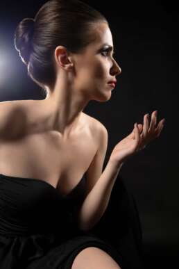 Portret profesional glamour al unei femei elegante în rochie neagră, profil iluminat artistic, fundal negru, lumină de studio