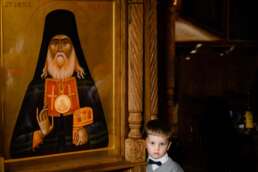Băiat mic într-o biserică ortodoxă, stând lângă icoana Sfântului Luca – contrast între copilărie și solemnitate religioasă, fotografie de botez București